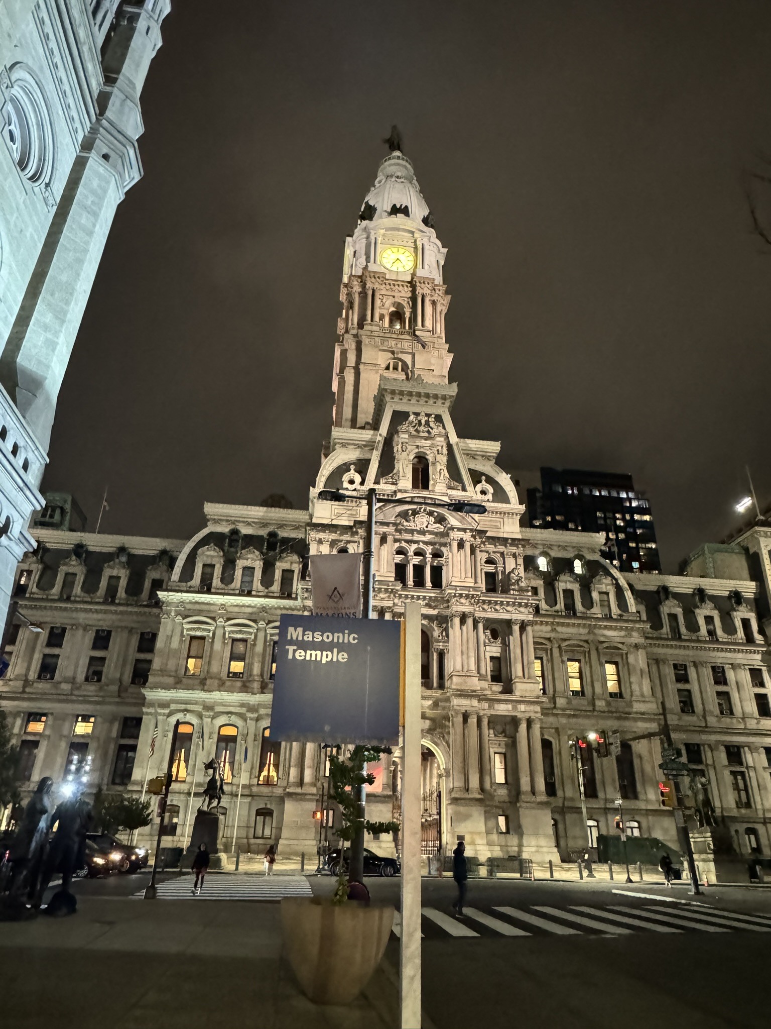 Illuminated civic-style tower rising above nearby buildings at night.